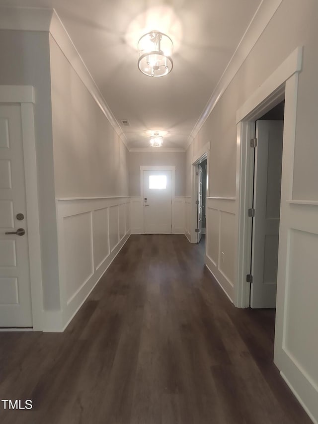 hallway with dark wood-style flooring, a wainscoted wall, crown molding, and a decorative wall