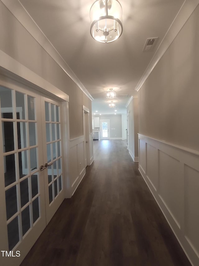 hall featuring visible vents, dark wood-style floors, a wainscoted wall, crown molding, and french doors