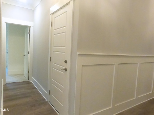 hall with a wainscoted wall, ornamental molding, a decorative wall, and dark wood-type flooring