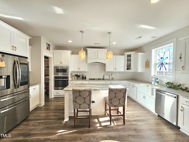 kitchen featuring appliances with stainless steel finishes, custom exhaust hood, pendant lighting, white cabinetry, and a kitchen island