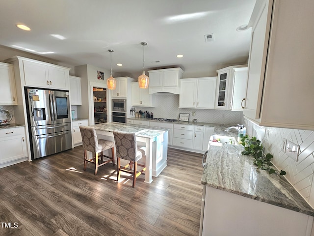 kitchen featuring dark hardwood / wood-style floors, light stone countertops, appliances with stainless steel finishes, a kitchen island, and white cabinetry