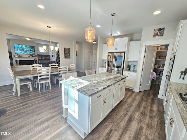 kitchen with white cabinets, hanging light fixtures, light stone countertops, a kitchen island, and stainless steel fridge with ice dispenser