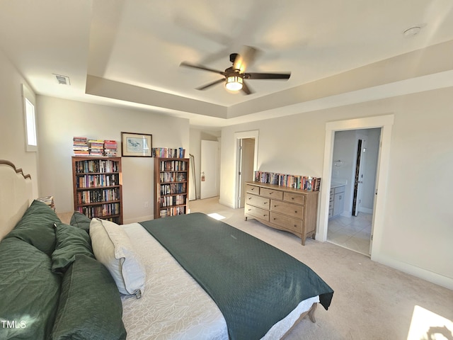 carpeted bedroom featuring a raised ceiling, connected bathroom, and ceiling fan