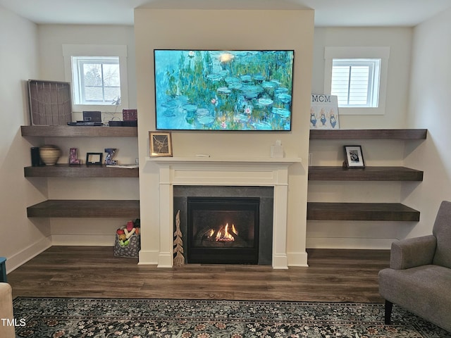 living room with a warm lit fireplace, baseboards, and wood finished floors