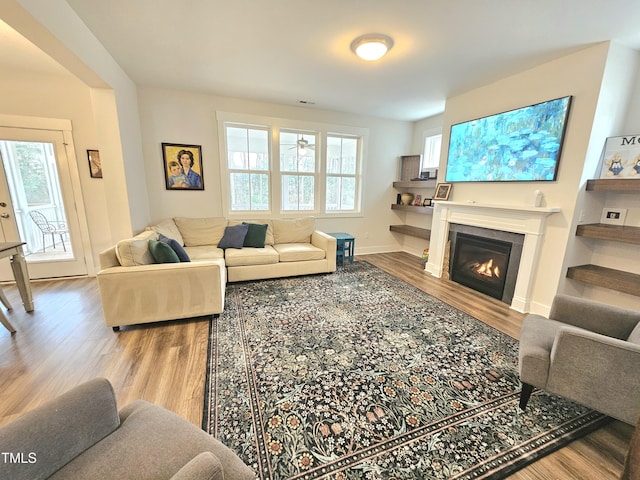 living area with a wealth of natural light, a lit fireplace, and wood finished floors