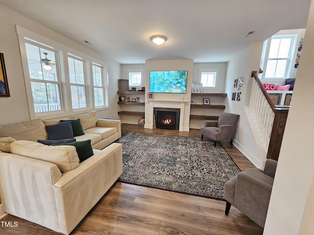 living area featuring a lit fireplace, wood finished floors, visible vents, and baseboards