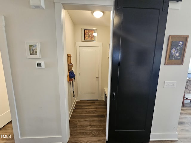 hall featuring a barn door, dark wood finished floors, and baseboards