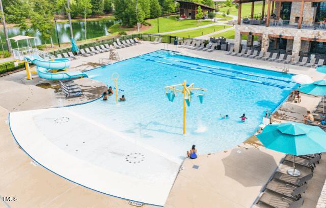 community pool featuring a patio area, a water play area, fence, and a water slide