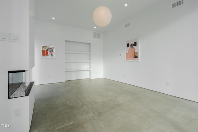 unfurnished living room with built in shelves and concrete flooring