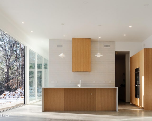 kitchen with pendant lighting, multiple ovens, light hardwood / wood-style flooring, and backsplash