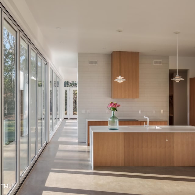 kitchen with a kitchen island with sink, hanging light fixtures, sink, and concrete floors