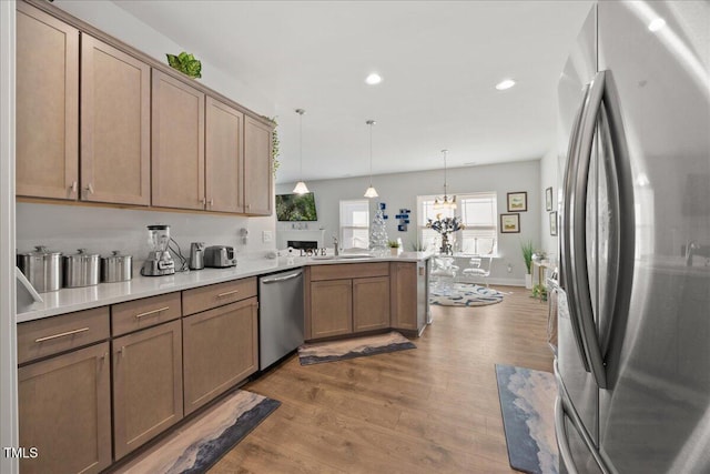 kitchen with kitchen peninsula, stainless steel appliances, wood-type flooring, a notable chandelier, and hanging light fixtures