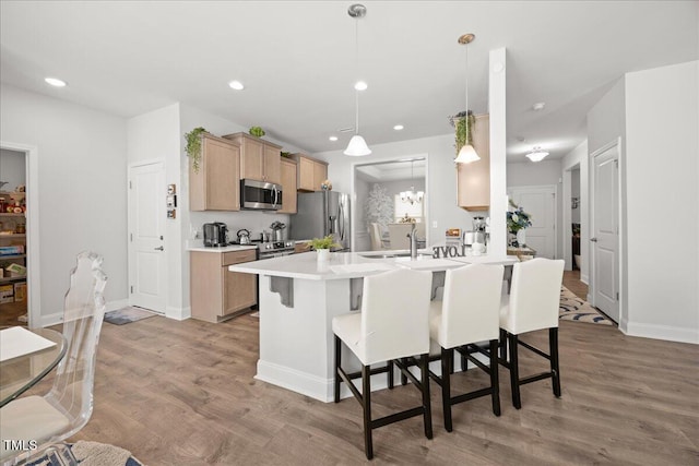 kitchen with kitchen peninsula, appliances with stainless steel finishes, a kitchen bar, light hardwood / wood-style flooring, and hanging light fixtures