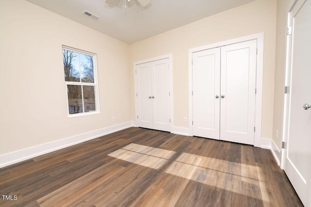 unfurnished bedroom with dark hardwood / wood-style flooring, ceiling fan, and multiple closets