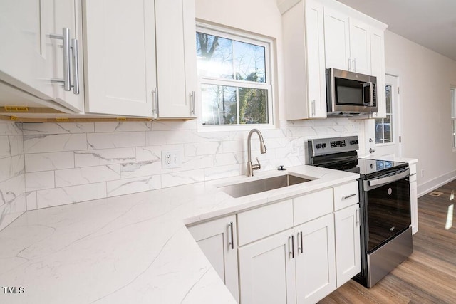 kitchen with light stone countertops, appliances with stainless steel finishes, sink, white cabinets, and light hardwood / wood-style floors