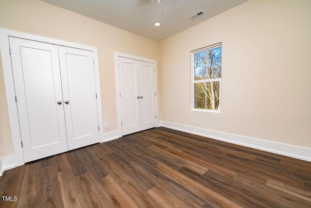 unfurnished bedroom featuring ceiling fan, dark hardwood / wood-style flooring, and two closets