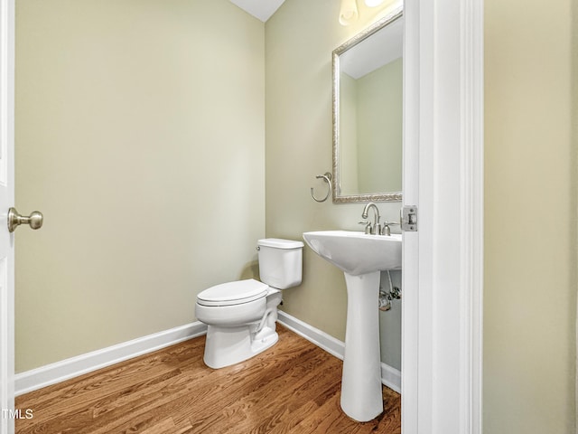 half bath featuring a sink, toilet, baseboards, and wood finished floors