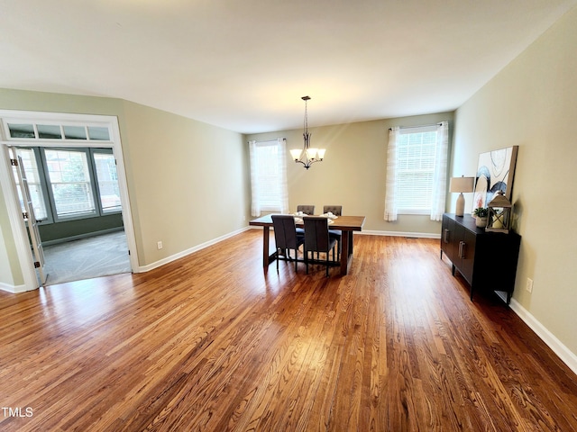 dining area featuring dark wood-type flooring, a chandelier, a healthy amount of sunlight, and baseboards