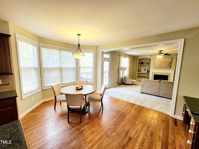 dining room featuring light wood-type flooring, built in shelves, a fireplace, and a healthy amount of sunlight