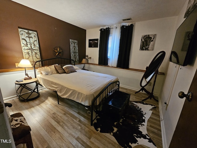 bedroom with a textured ceiling, wood finished floors, visible vents, and baseboards