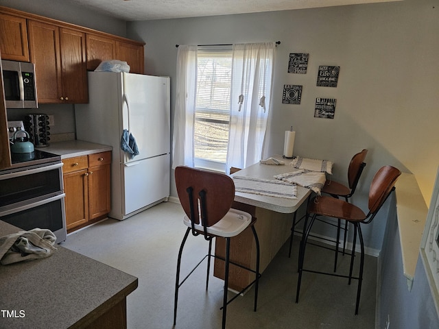 kitchen with stainless steel appliances, baseboards, brown cabinets, and a kitchen breakfast bar