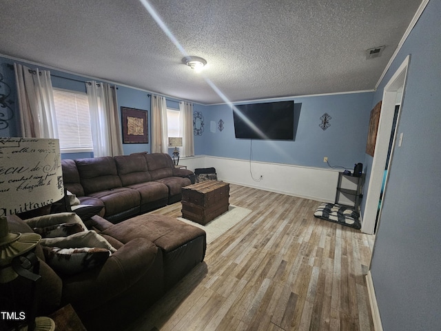 living area featuring ornamental molding, visible vents, a textured ceiling, and wood finished floors