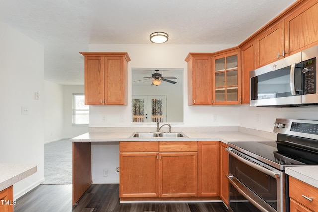 kitchen featuring glass insert cabinets, dark wood-type flooring, stainless steel appliances, light countertops, and a sink