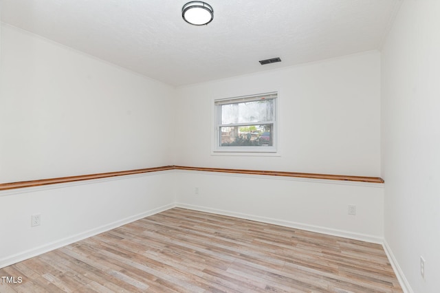 spare room with light wood finished floors, visible vents, baseboards, crown molding, and a textured ceiling