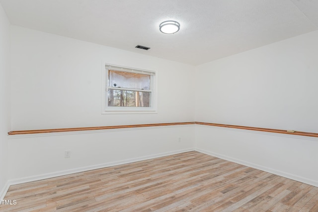 empty room with visible vents, a textured ceiling, baseboards, and wood finished floors