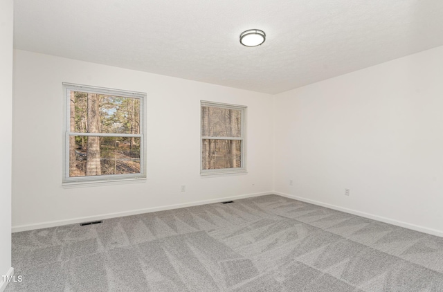 unfurnished room featuring a textured ceiling, carpet flooring, visible vents, and baseboards