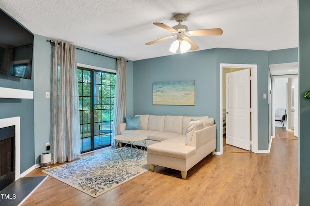 living room with ceiling fan, light wood-type flooring, and a textured ceiling