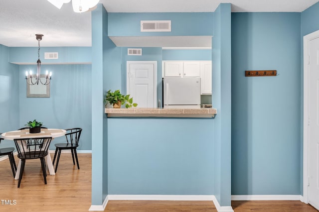 interior space with hanging light fixtures, light hardwood / wood-style flooring, white fridge, a chandelier, and white cabinets