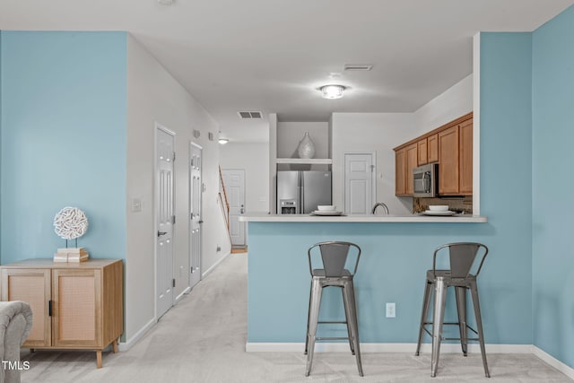 kitchen featuring a breakfast bar, light colored carpet, kitchen peninsula, and stainless steel appliances