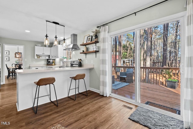 kitchen featuring a breakfast bar area, kitchen peninsula, white cabinetry, decorative light fixtures, and range hood