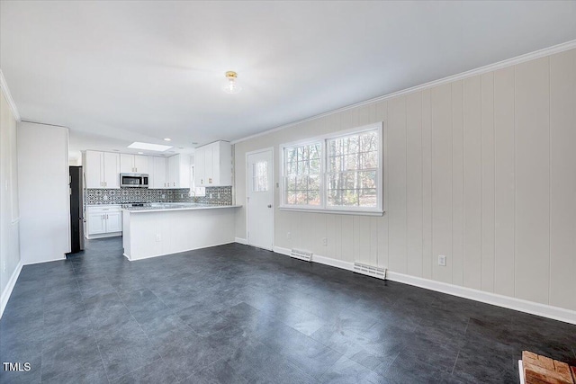 kitchen featuring kitchen peninsula, ornamental molding, appliances with stainless steel finishes, tasteful backsplash, and white cabinetry