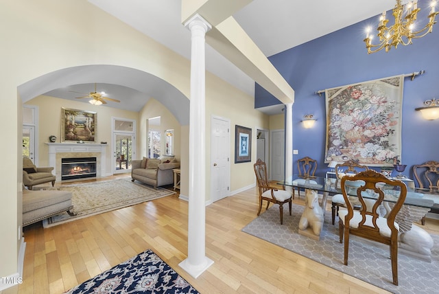 dining room with decorative columns, a towering ceiling, ceiling fan, and light wood-type flooring