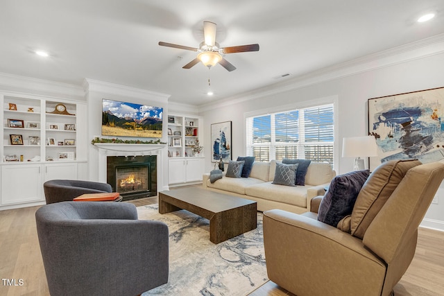 living room featuring built in shelves, a premium fireplace, light hardwood / wood-style flooring, and ceiling fan