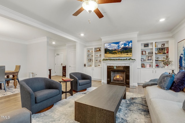 living room with ceiling fan, built in features, light wood-type flooring, and ornamental molding