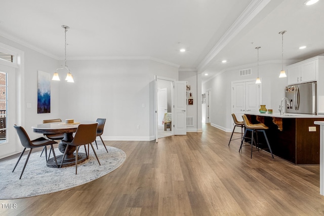 dining space featuring an inviting chandelier, light hardwood / wood-style flooring, ornamental molding, and sink