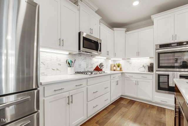 kitchen with white cabinets, decorative backsplash, appliances with stainless steel finishes, and light hardwood / wood-style flooring