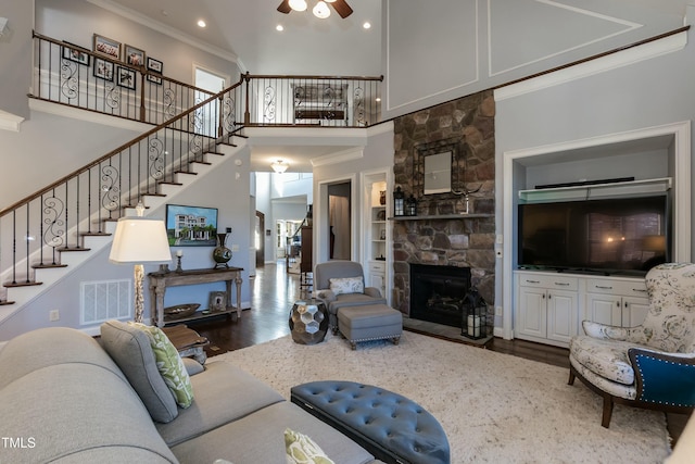 living room with a high ceiling, a fireplace, built in features, wood-type flooring, and crown molding