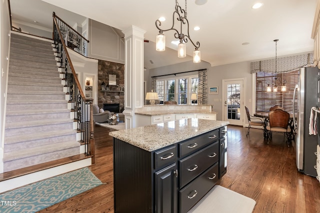 kitchen featuring an inviting chandelier, a fireplace, stainless steel refrigerator, a kitchen island, and pendant lighting