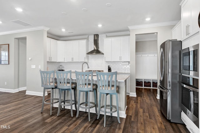 kitchen featuring white cabinets, wall chimney exhaust hood, stainless steel appliances, and an island with sink