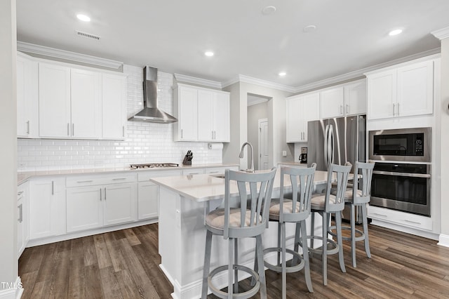 kitchen featuring white cabinets, wall chimney range hood, and appliances with stainless steel finishes