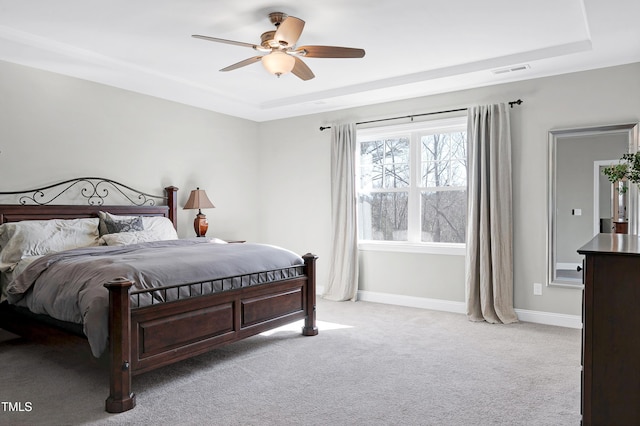 bedroom with a raised ceiling, ceiling fan, and light colored carpet