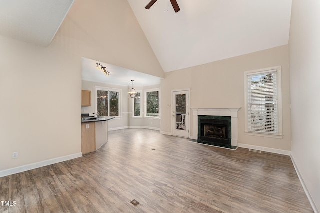 unfurnished living room with dark wood-type flooring, a high end fireplace, ceiling fan with notable chandelier, and high vaulted ceiling