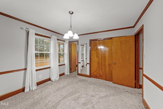 carpeted empty room with crown molding, a textured ceiling, and an inviting chandelier