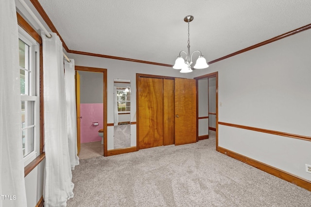 interior space featuring carpet flooring, ornamental molding, a textured ceiling, and an inviting chandelier