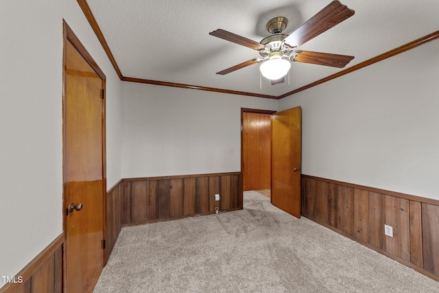 spare room featuring light carpet, crown molding, ceiling fan, and a textured ceiling