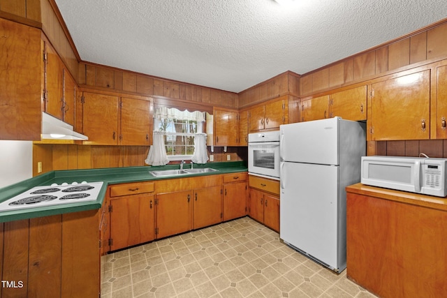 kitchen featuring a textured ceiling, wood walls, sink, and white appliances